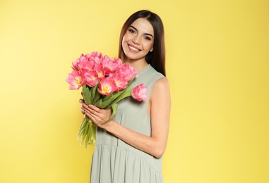 Photo of Portrait of beautiful smiling girl with spring tulips on yellow background. International Women's Day