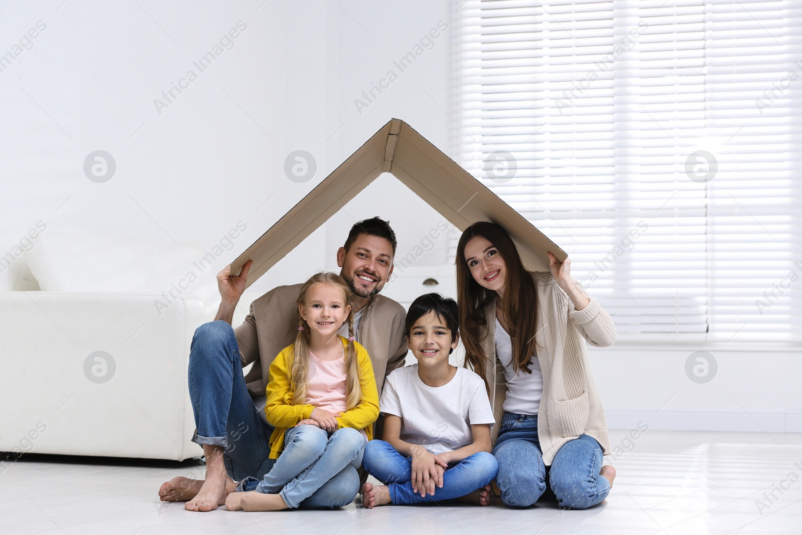 Photo of Happy family sitting under cardboard roof at home. Insurance concept