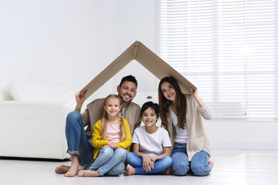 Happy family sitting under cardboard roof at home. Insurance concept