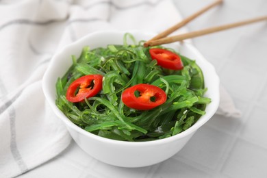 Photo of Tasty seaweed salad served in bowl on white tiled table, closeup