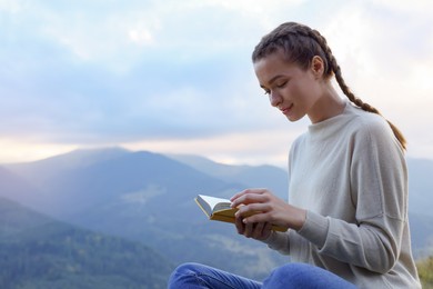 Photo of Beautiful young woman reading book in mountains, space for text