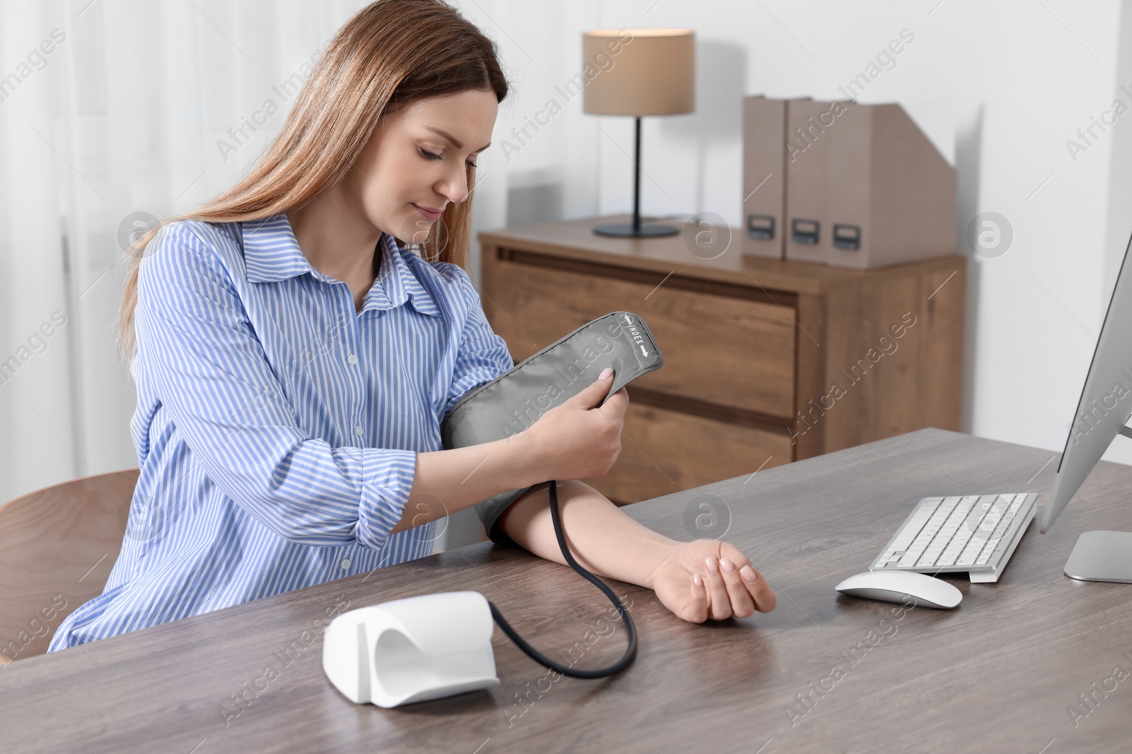 Photo of Woman measuring blood pressure at wooden table in room, space for text