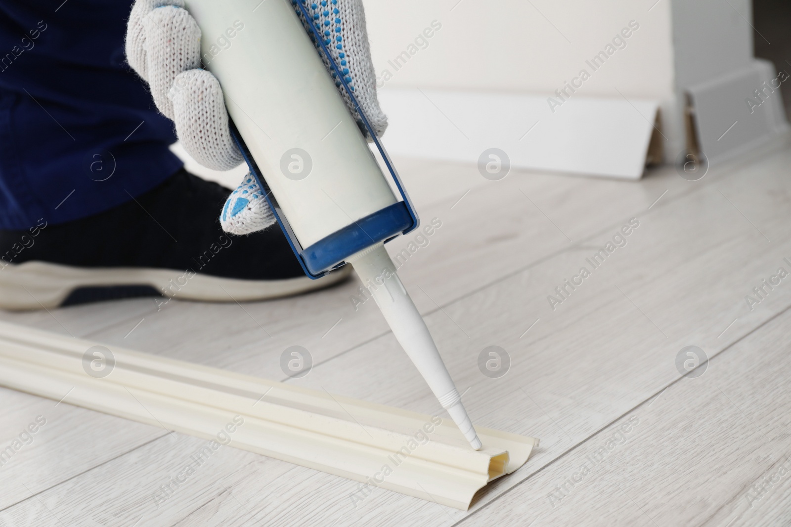 Photo of Man using caulking gun while installing plinth on laminated floor in room, closeup