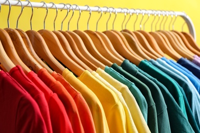 Photo of Rack with bright clothes on yellow background. Rainbow colors