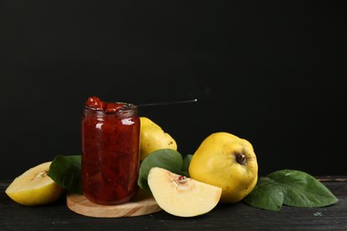 Photo of Delicious quince jam and fruits on black wooden table