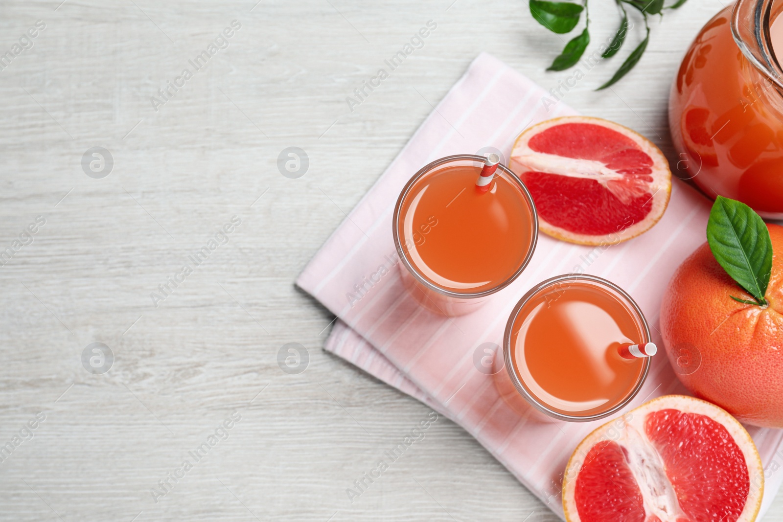 Photo of Tasty freshly made grapefruit juice and fruits on white wooden table, flat lay. Space for text