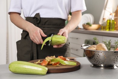 Woman peeling fresh zucchini at light table indoors, closeup