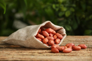 Photo of Fresh unpeeled peanuts in sack on wooden table against blurred background
