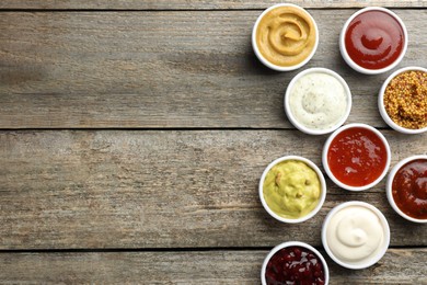 Photo of Different tasty sauces in bowls on wooden table, flat lay. Space for text
