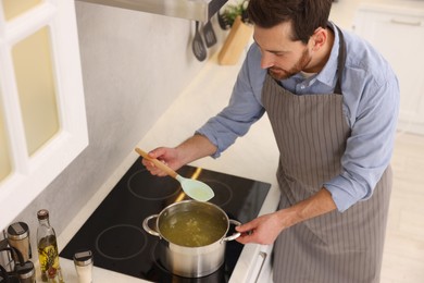 Photo of Man cooking delicious chicken soup in kitchen, above view