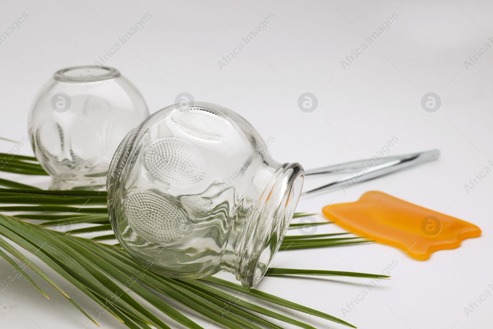 Photo of Glass cups, tweezers, gua sha and leaf on light grey background, closeup. Cupping therapy