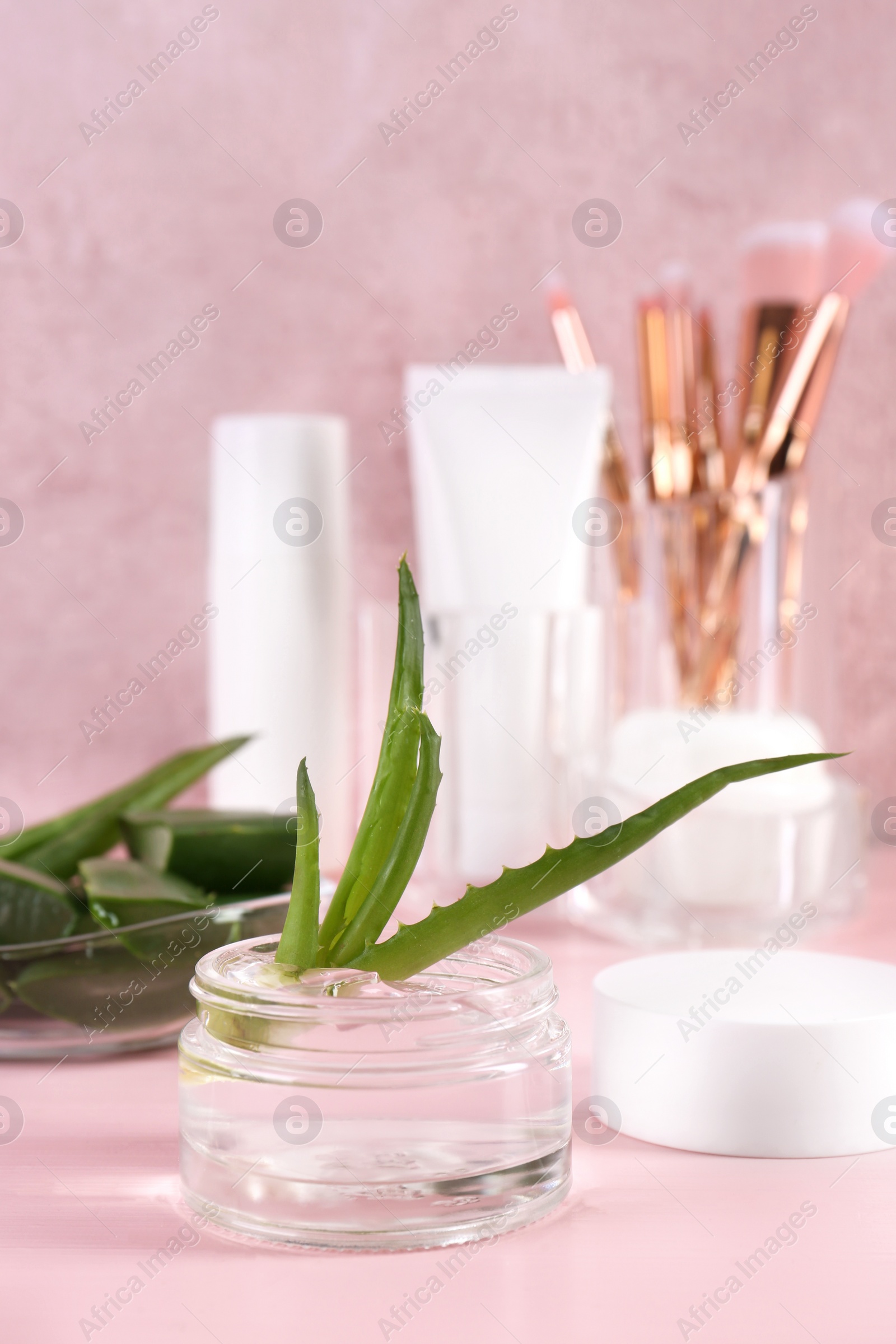 Photo of Jar of natural gel and aloe vera leaves on pink table