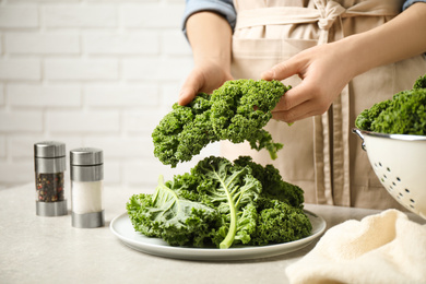 Photo of Woman holding fresh kale leaves over light grey table, closeup