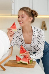 Photo of Beautiful teenage girl eating watermelon at countertop in kitchen