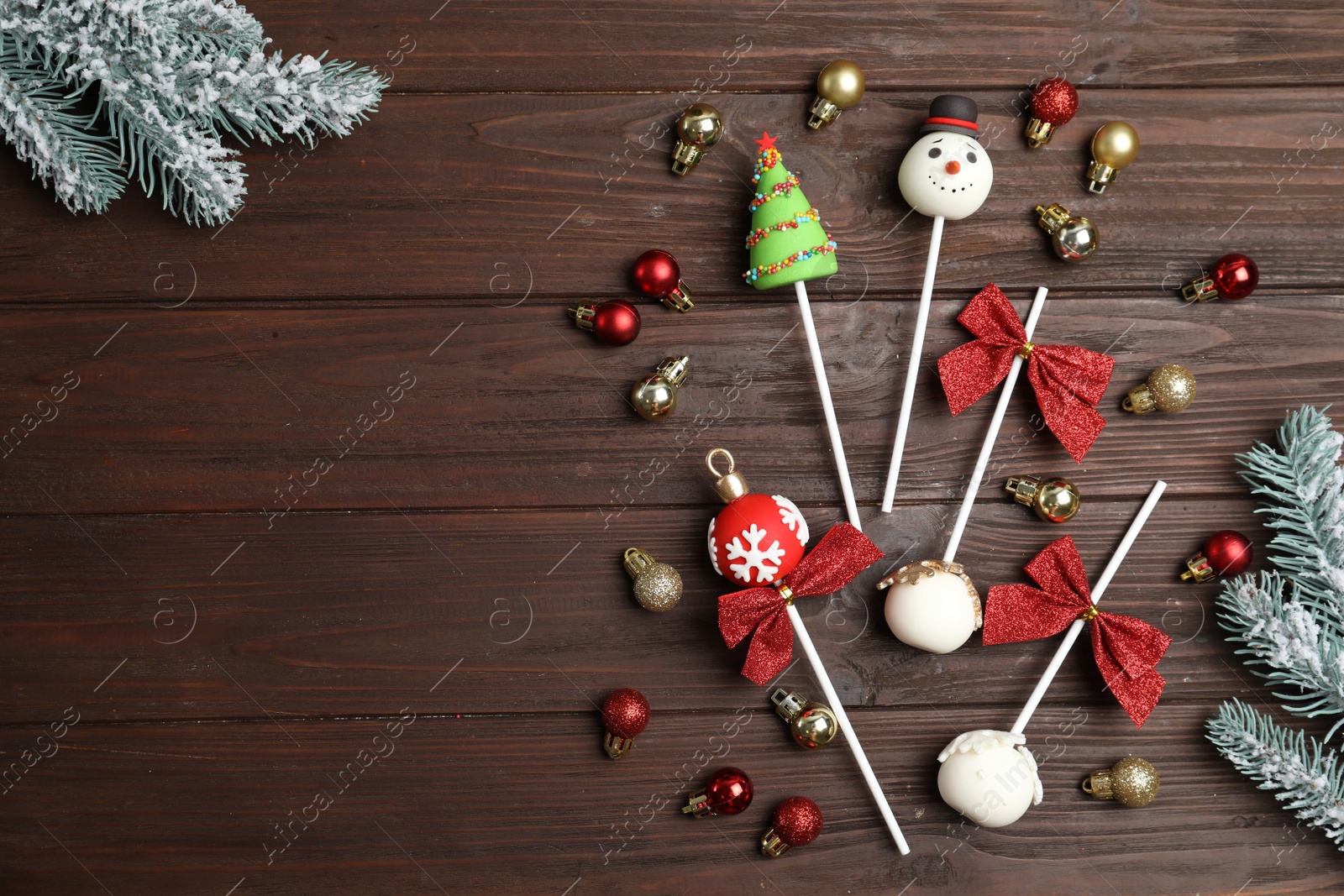 Photo of Delicious Christmas themed cake pops with fir tree branches and balls on wooden table, flat lay. Space for text
