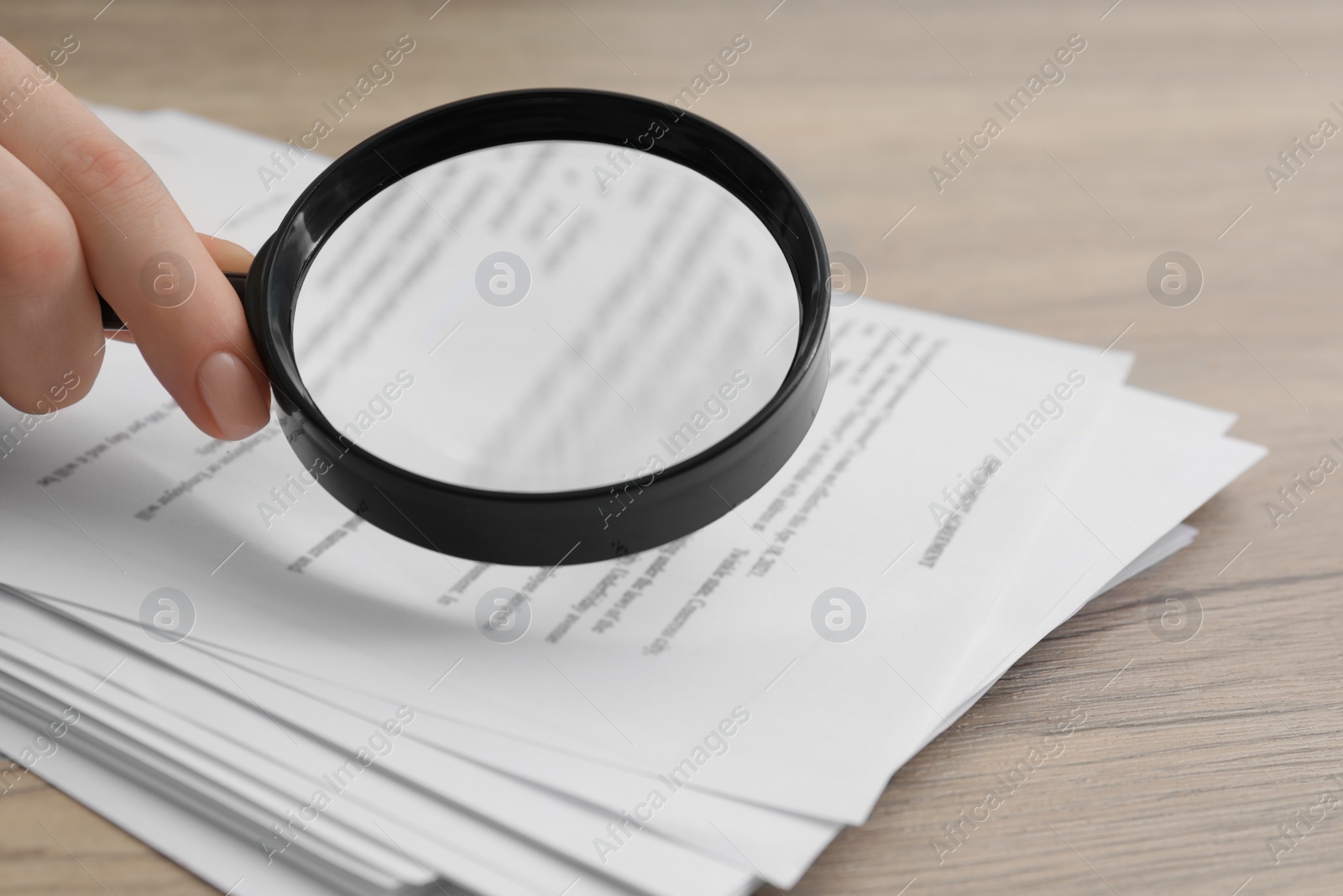 Photo of Woman looking at document through magnifier at wooden table, closeup. Searching concept