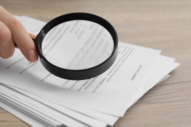 Woman looking at document through magnifier at wooden table, closeup. Searching concept