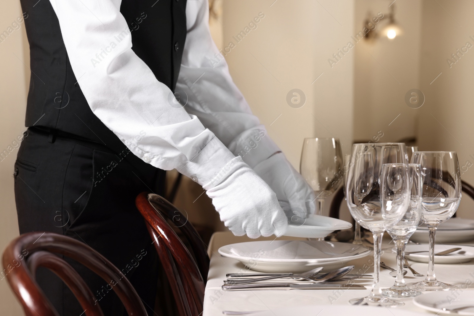 Photo of Man setting table in restaurant, closeup. Professional butler courses