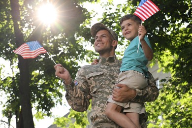 Photo of Soldier and his little son with American flags outdoors, low angle view. Veterans Day in USA