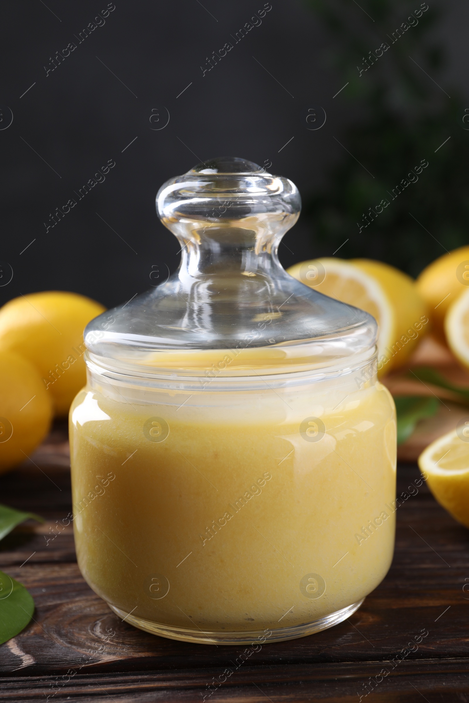 Photo of Delicious lemon curd in glass jar and fresh citrus fruits on wooden table