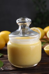 Delicious lemon curd in glass jar and fresh citrus fruits on wooden table