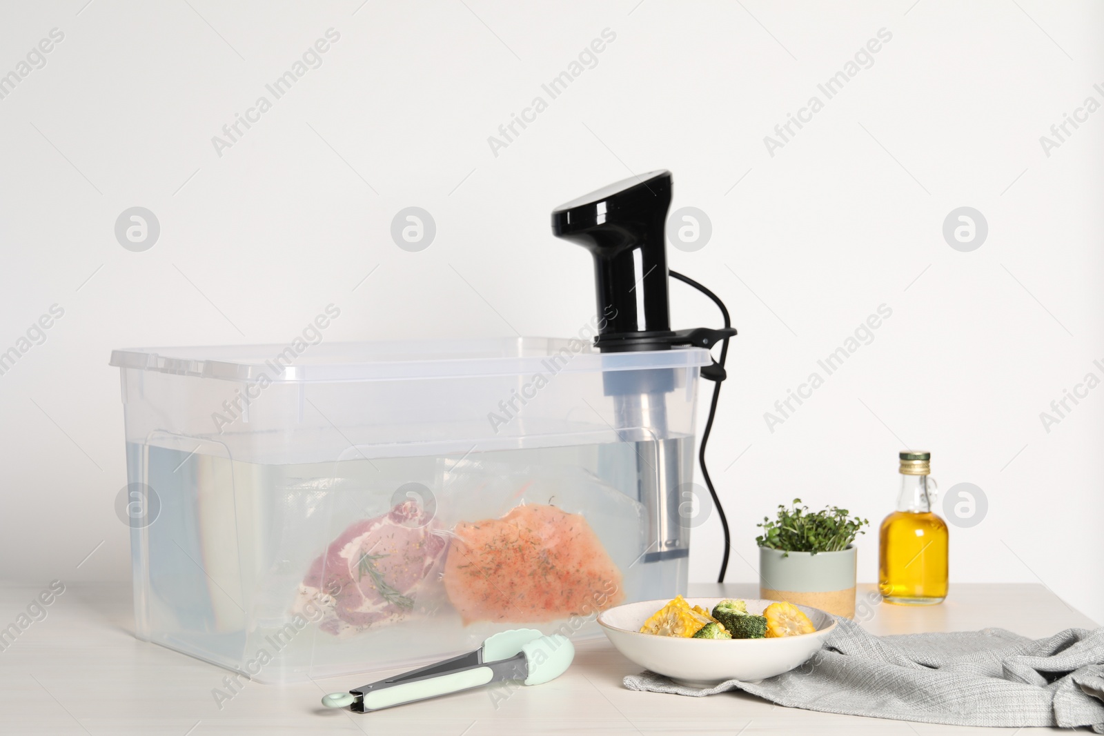 Photo of Thermal immersion circulator and vacuum packed meat in box on white wooden table. Sous vide cooking