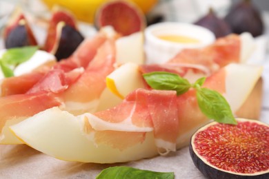 Photo of Tasty melon, jamon and figs served on wooden board, closeup
