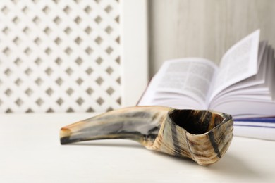 Photo of Shofar and open Torah on white wooden table, space for text. Rosh Hashanah holiday symbols