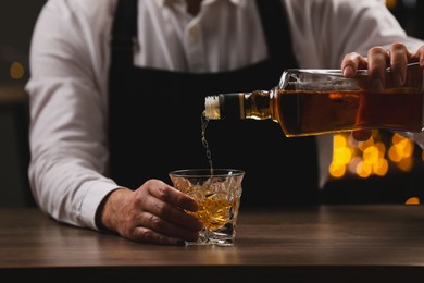 Photo of Bartender pouring whiskey from bottle into glass at bar counter indoors, closeup