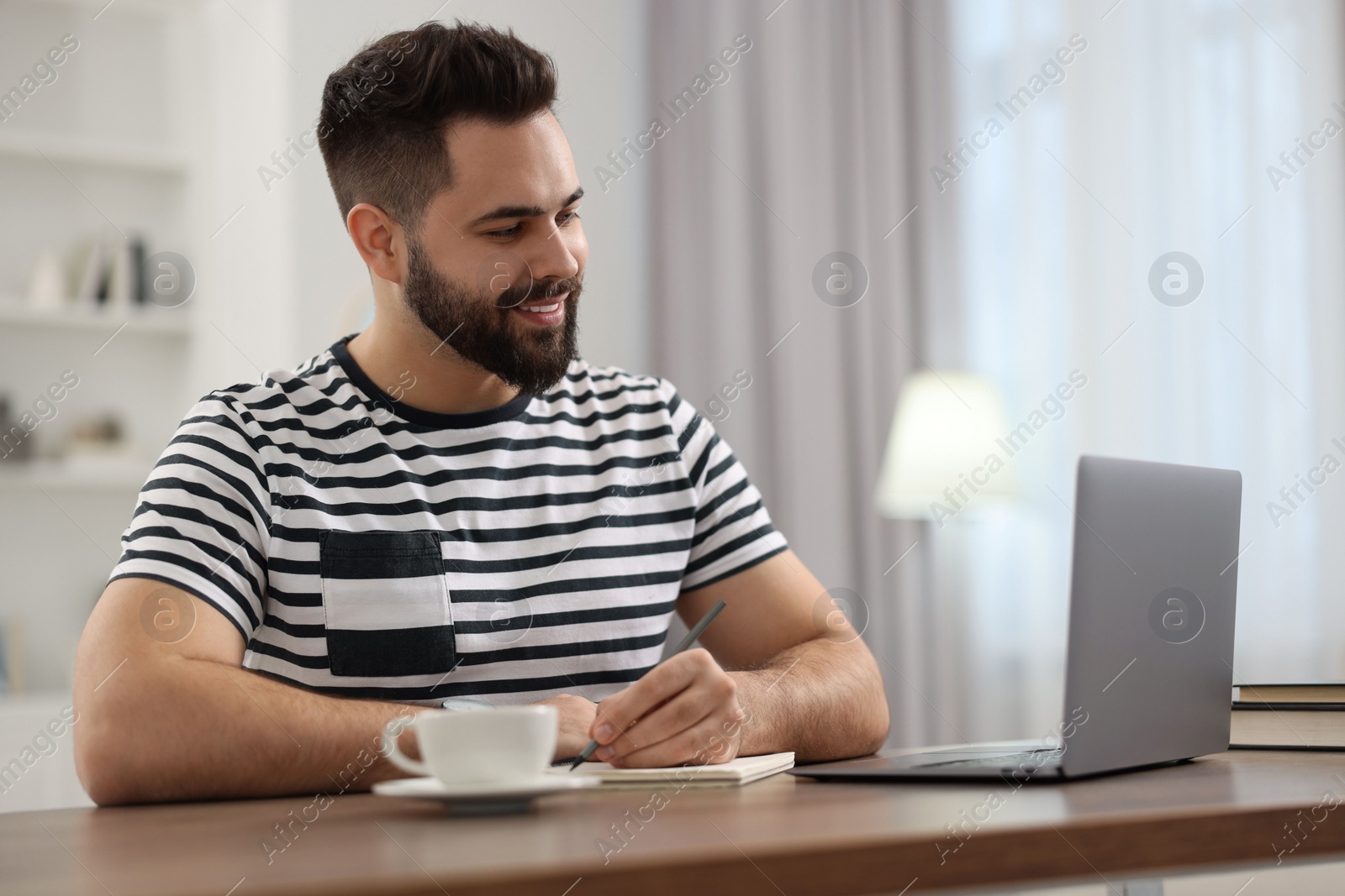 Photo of Young man watching webinar at table in room