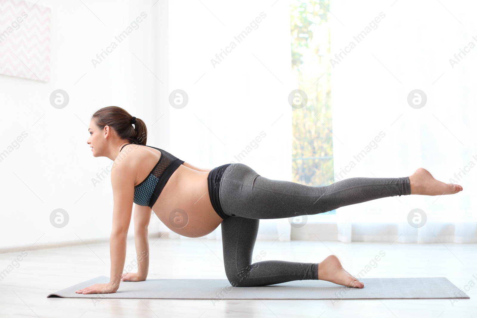 Photo of Young pregnant woman in fitness clothes practicing yoga at home