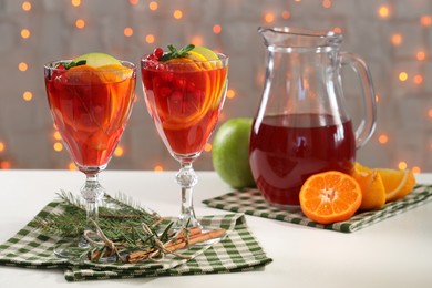 Photo of Christmas Sangria cocktail in glasses and jug, ingredients and fir tree branch on white table against blurred lights