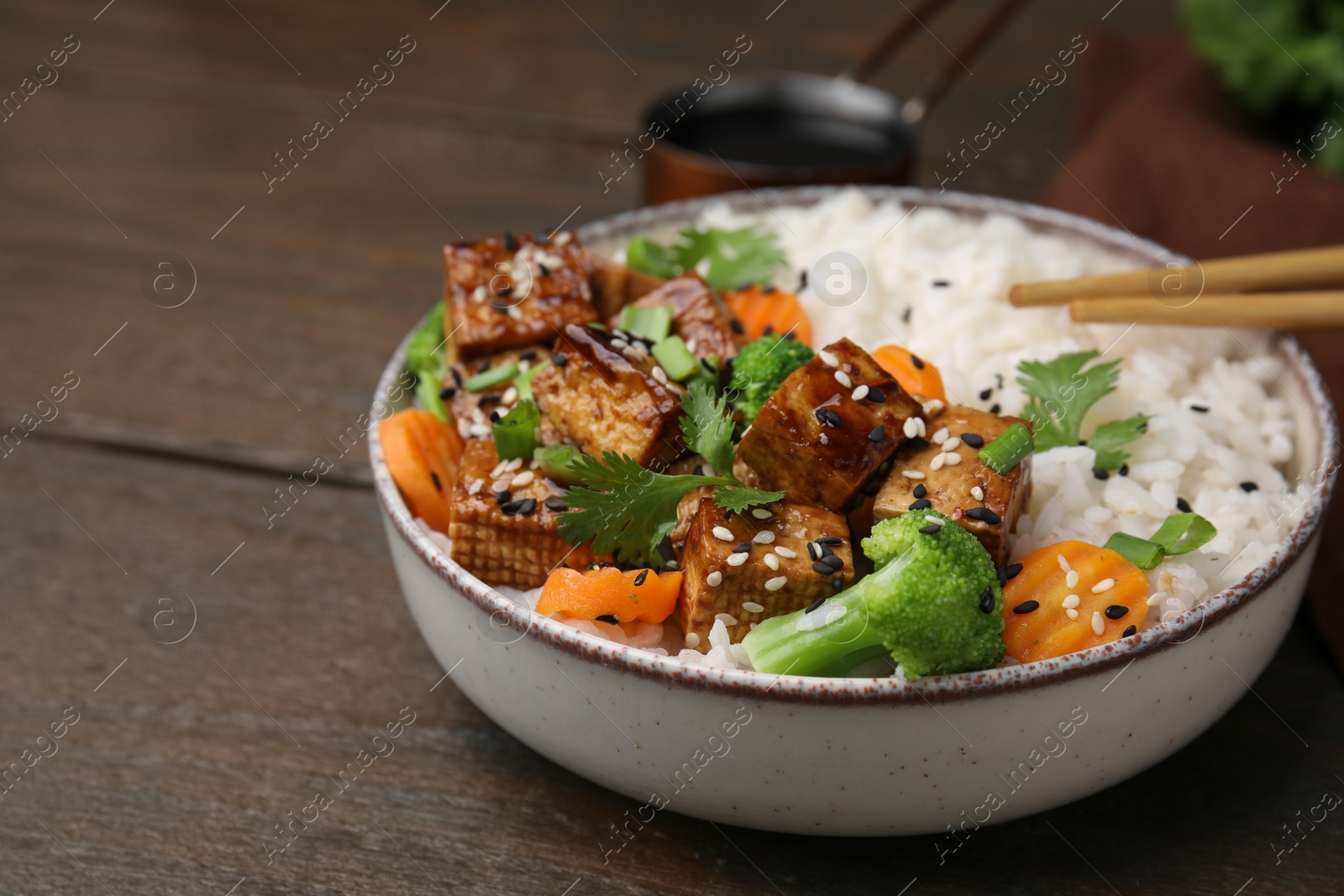 Photo of Bowl of rice with fried tofu, broccoli and carrots on wooden table, closeup. Space for text