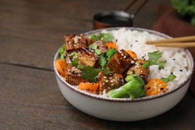 Photo of Bowl of rice with fried tofu, broccoli and carrots on wooden table, closeup. Space for text
