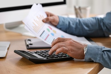 Photo of Professional accountant using calculator at wooden desk, closeup