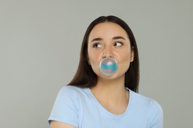 Beautiful woman blowing bubble gum on grey background