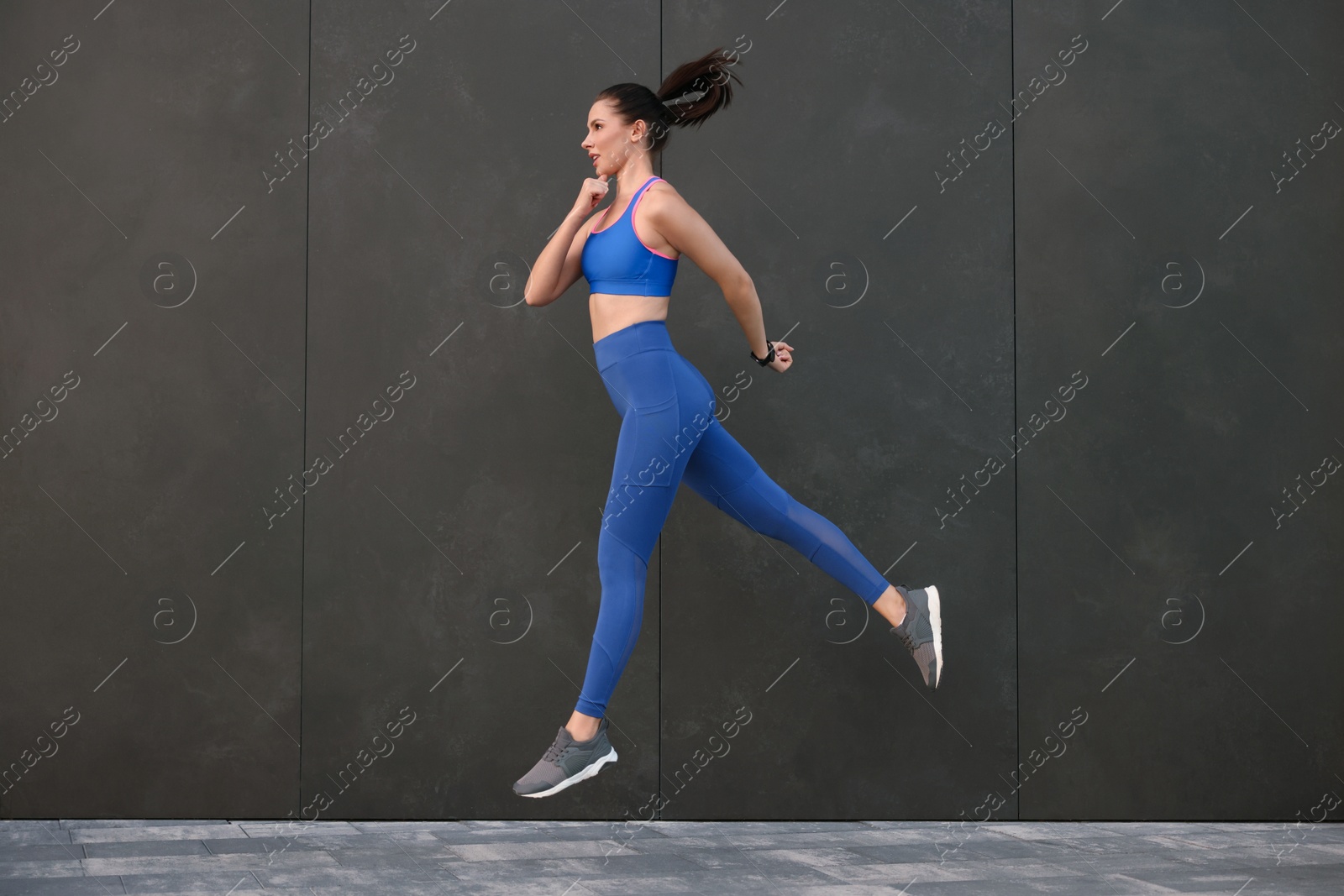 Photo of Beautiful woman in stylish sportswear jumping near black wall outdoors