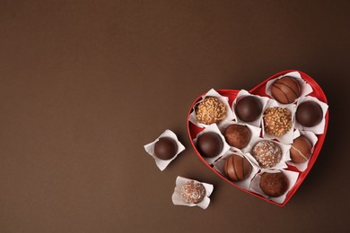 Photo of Heart shaped box with delicious chocolate candies on brown background, flat lay. Space for text