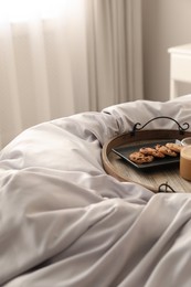 Photo of Delicious cookies and cup of coffee on bed with stylish silky linens indoors, space for text
