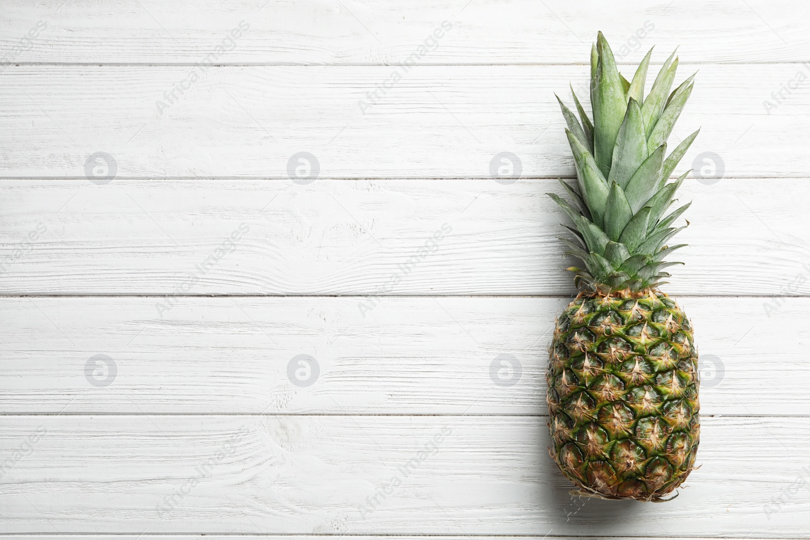 Photo of Fresh whole pineapple on white wooden background, top view. Space for text