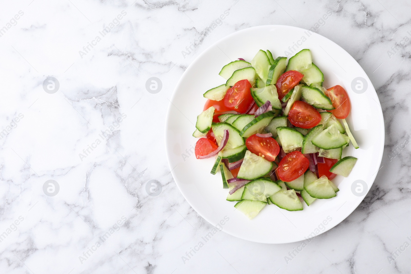 Photo of Plate of vegetarian salad with cucumber, tomato and onion on marble background, top view. Space for text