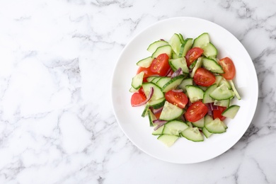 Photo of Plate of vegetarian salad with cucumber, tomato and onion on marble background, top view. Space for text