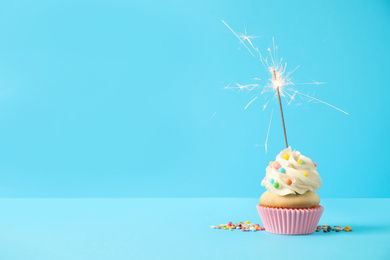 Photo of Birthday cupcake with sparkler on light blue background. Space for text