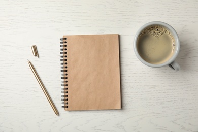 Notebook and cup of coffee on wooden background, top view