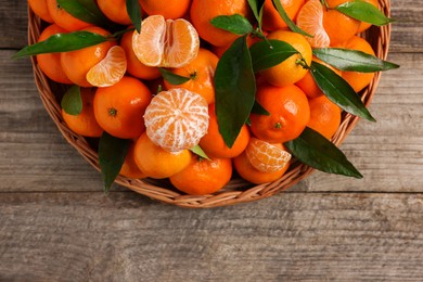 Fresh ripe juicy tangerines and green leaves on wooden table, top view. Space for text
