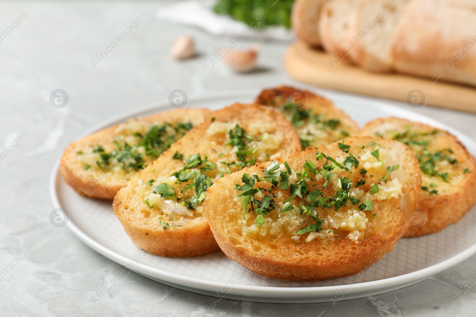 Photo of Slices of toasted bread with garlic and herb on light grey marble table, closeup