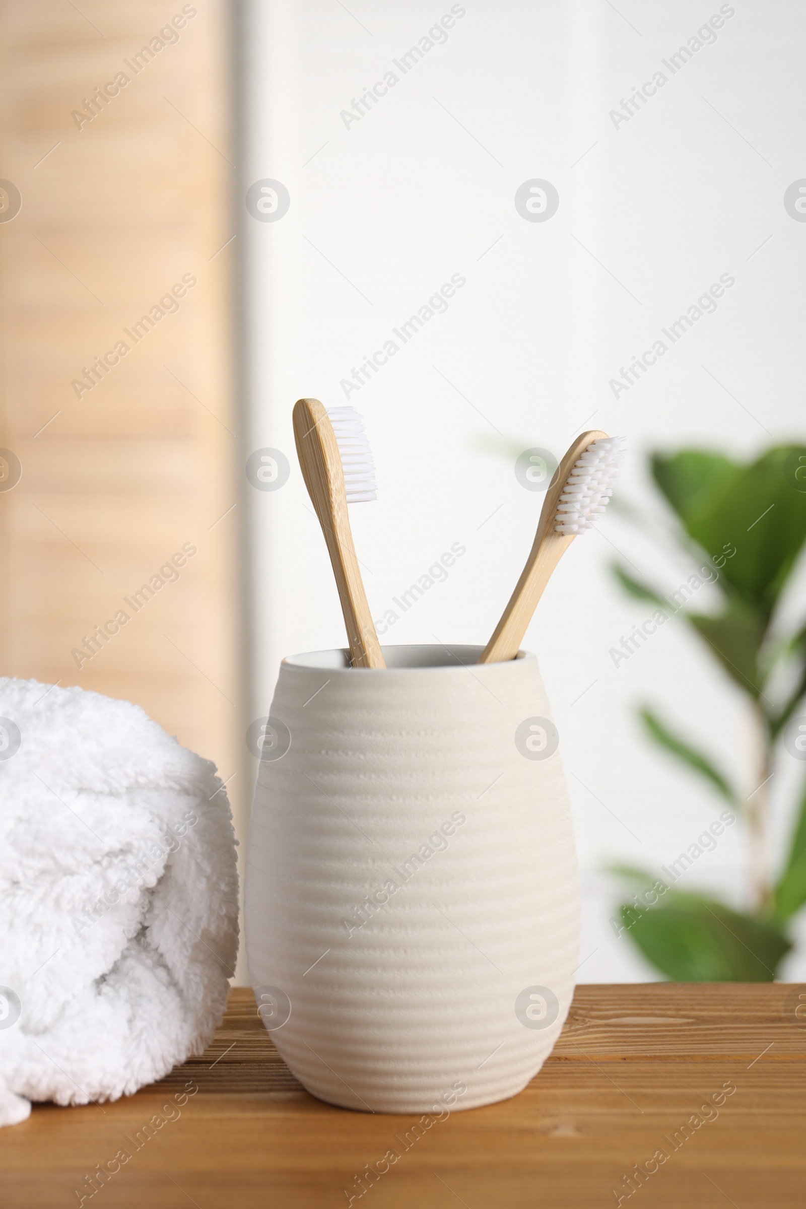 Photo of Holder with bamboo toothbrushes and towel on wooden table in bathroom