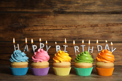 Birthday cupcakes with burning candles on table against wooden background. Space for text