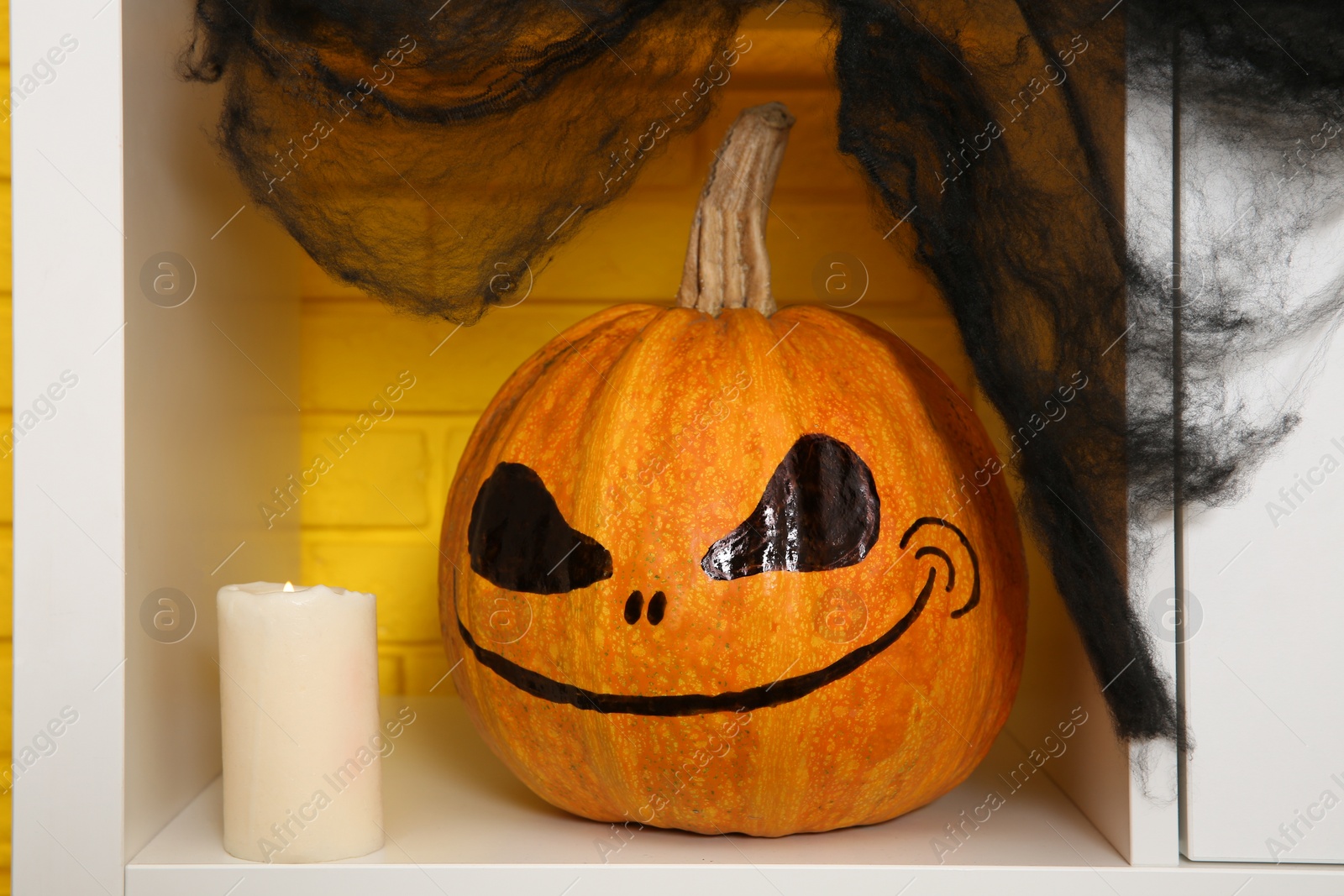 Photo of Pumpkin with drawn spooky face and candle on shelf. Halloween decor