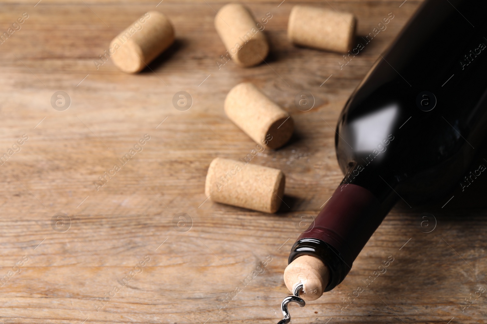 Photo of Opening wine bottle with corkscrew on wooden table, closeup. Space for text